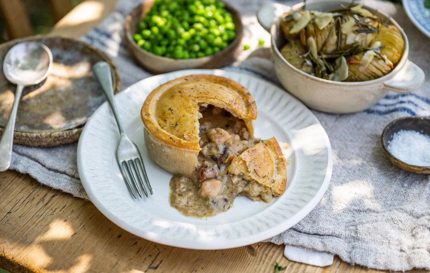Chicken and bacon pie with a golden puff pastry lid, cut to reveal creamy chicken and smoky bacon filling, served with mash and peas