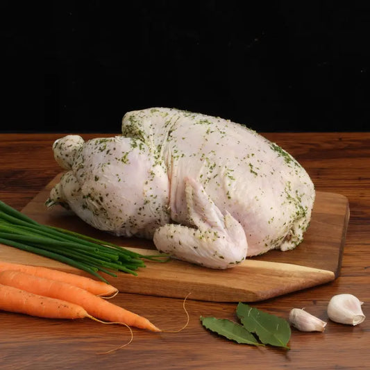 Raw chicken on a wooden cutting board with carrots and herbs on a dark background