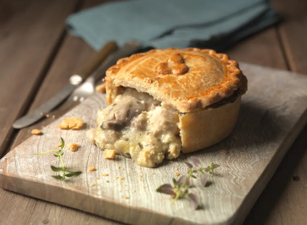 Chicken and mushroom pie with a golden puff pastry lid, cut to reveal creamy chicken and mushroom filling, served with mash and greens