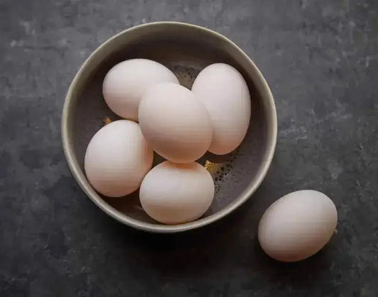 Duck eggs in a carton with one cracked to show a deep golden yolk, ready for poaching or baking