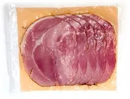 Honey roasted sliced ham layered on a board with mustard, pickles and crusty bread, ready for sandwiches