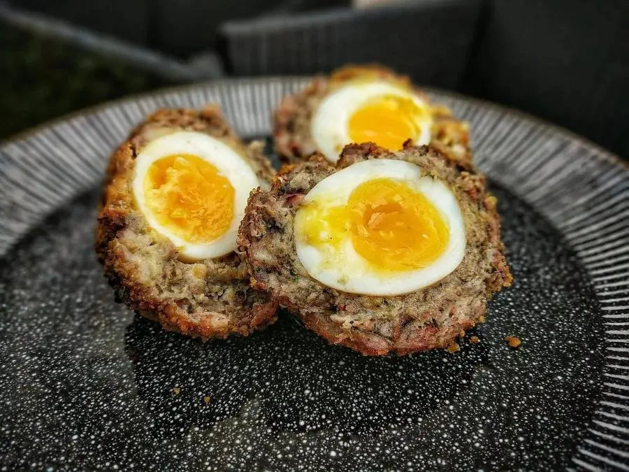 Pulled pork scotch egg halved to show a jammy yolk, with smoky pulled pork and sausage layer under a crisp golden crumb