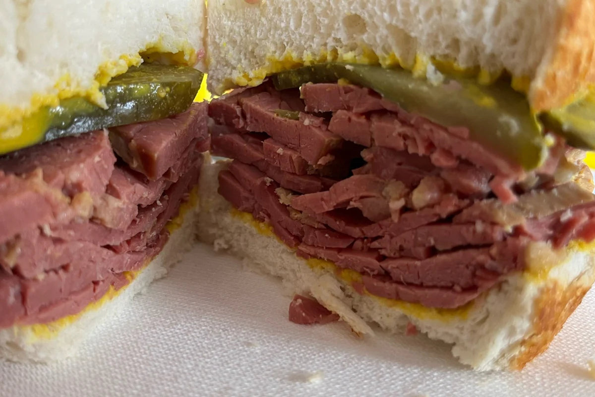 Salt beef roll baked to a golden flaky crust, sliced to show the tender cured beef filling with mustard and pickles on the side