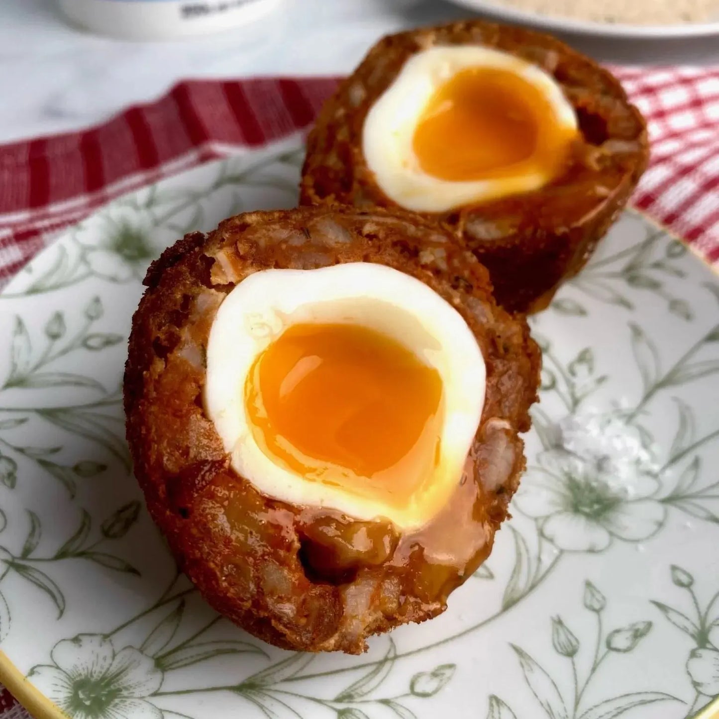Spicy chorizo scotch egg halved to show a jammy yolk, with a crisp golden crumb and paprika-red sausage layer